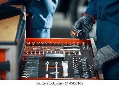 Close-up image of car service worker in gloves taking ratchet for socket wrench out of drawer when repairing automobile in garage