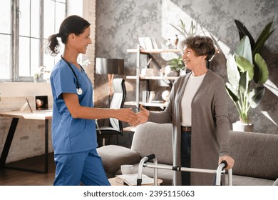 Closeup image of caregiver nurse caretaker doctor greeting giving handshake to senior old elderly grandmother patient female with walking frame with motion immobility in hospice at home. Homecare - Shutterstock ID 2395115063
