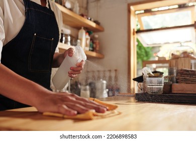 Closeup Image Of Coffeeshop Owner Sparying Detergent On Counter And Wiping With Soft Cloth