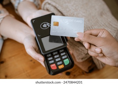 A close-up image of a customer tapping her credit card with a payment terminal or credit card machine at a cashier in a clothing store. cashless payment, card reader, electronic funds transfer