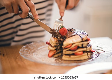 Close-up image with delicious pancakes stack cut with some elegant cutlery knife, gourmet homemade pancakes on the plate with fresh strawberries and chocolate
