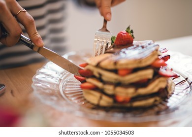 Close-up image with delicious pancakes stack cut with some elegant cutlery knife, gourmet homemade pancakes on the plate with fresh strawberries and chocolate