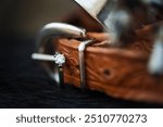 Closeup image of a diamond and emerald wedding ring resting on the buckle of a leather spur. 