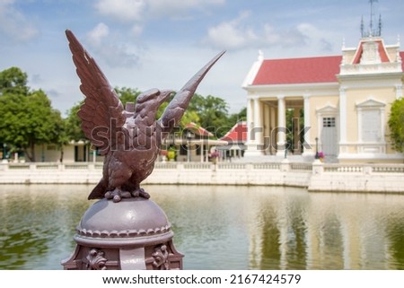 The closeup image of eagle statue. The bokeh background is The Phra Thinang Warophat Phiman or “Excellent and Shining Heavenly Abode” in Bang Pa-In Palace Ayutthaya Thailand. 