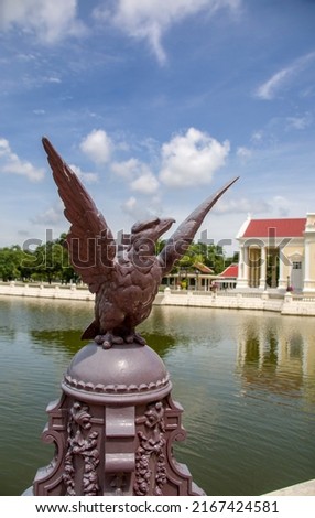 The closeup image of eagle statue. The bokeh background is The Phra Thinang Warophat Phiman or “Excellent and Shining Heavenly Abode” in Bang Pa-In Palace Ayutthaya Thailand. 