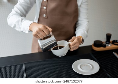 A close-up image of an experienced female barista pouring milk into a coffee cup, preparing customer's orders, working in a coffee shop. - Powered by Shutterstock