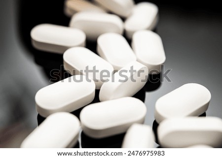 Close-up image featuring a row of white, oval-shaped pills scattered on a dark, reflective surface. These may represent opioids, highlighting issues related to medical use and overdose risks.