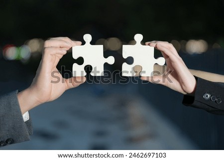 Close-up image featuring two professionals holding large jigsaw puzzle pieces, representing collaboration, problem-solving, and partnership towards a common goal in a corporate setting
