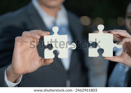 Close-up image featuring two professionals holding large jigsaw puzzle pieces, representing collaboration, problem-solving, and partnership towards a common goal in a corporate setting