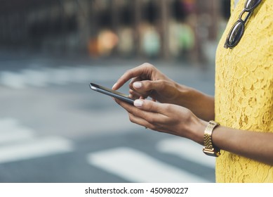 Close-up image of female hands using modern smart phone outside, woman'?s hands typing on touch screen of cellphone while standing at crosswalk in the city