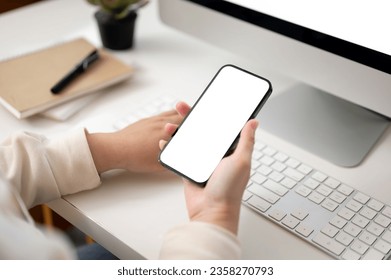 Close-up image of a female office worker using her smartphone while working on her computer at her desk in the office. smartphone white screen mockup - Powered by Shutterstock