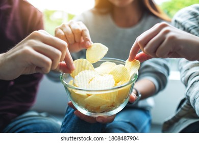 Closeup Image Of Friends Sharing And Eating Potato Chips At Home Party Together