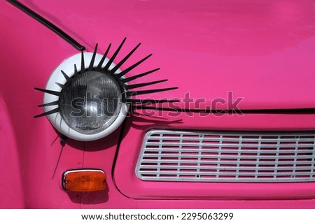 Closeup image of the front part of the pink customized car with a head lamp decorated with eyelashes