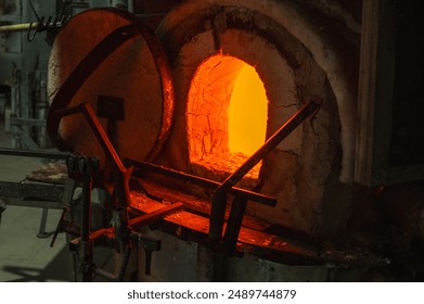 Close-up image of a glassblower forming hot molten glass under intense fire in a workshop, blast furnace. Manual processing of glass by masters inside the glass. Selective focus - Powered by Shutterstock