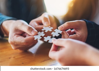 Closeup Image Of A Group Of People Holding And Putting A Piece Of White Jigsaw Puzzle Together