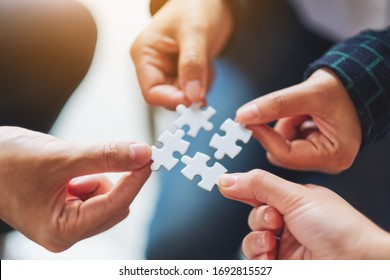 Closeup image of a group of people holding and putting a piece of white jigsaw puzzle together - Shutterstock ID 1692815527