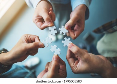 Closeup Image Of A Group Of People Holding And Putting A Piece Of White Jigsaw Puzzle Together