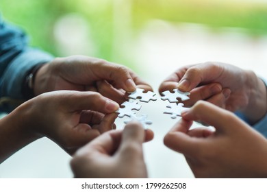 Closeup Image Of A Group Of People Holding And Putting A Piece Of White Jigsaw Puzzle Together