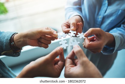 Closeup Image Of A Group Of People Holding And Putting A Piece Of White Jigsaw Puzzle Together