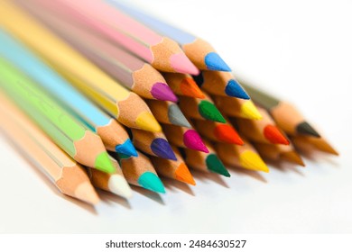 A close-up image of a group of wooden colored pencils arranged in a triangular pattern with the sharpened ends pointing up on a white background. - Powered by Shutterstock