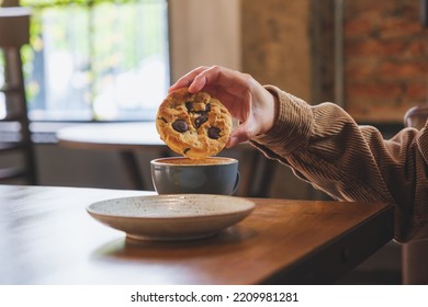 Closeup Image Of A Hand Holding And Dipping A Chocolate Chip Cookie Into Hot Drinks