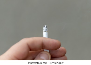 Close-up Image Of A Hand Holding A Lit Marijuana Joint Against Dark Gray Background