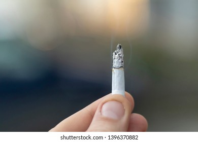 Close-up Image Of A Hand Holding A Lit Marijuana Joint Against Dark Gray Background