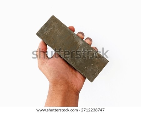 A close-up image of a hand holding a rectangular sharpening stone, showing its rough surface and natural texture, commonly used for sharpening knives and other cutting tools.