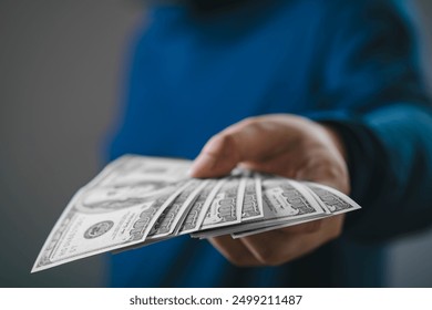 A close-up image of a hand offering multiple U.S. dollar bills, signifying financial transaction, loan, or payment in a business context.
