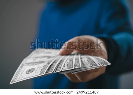 A close-up image of a hand offering multiple U.S. dollar bills, signifying financial transaction, loan, or payment in a business context.