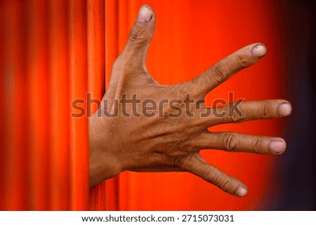 A close-up image of a hand reaching through vibrant orange bars, showcasing the unique texture of skin and nails. This striking visual emphasizes a sense of yearning and creativity.