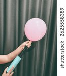 A close-up image of a hand, skillfully pumping air into a colorful balloon, showcasing the delicate interaction between fingers and the rubber material, the balloon slowly inflating.