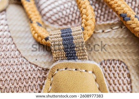 Close-up image of a handle and strap area of outdoor gear or luggage, with textured fabric, stitching details, and a blurred background suggesting a collection of outdoortravel items