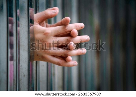 A close-up image of hands intertwined between metal bars, showcasing emotion and depth. The contrast of texture and light creates a captivating visual narrative.
