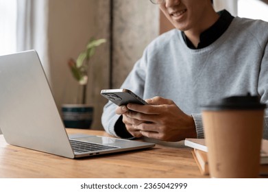 Close-up image of a handsome and happy young Asian man in casual clothes using his smartphone while working remotely at a coffee shop on the weekend. - Powered by Shutterstock