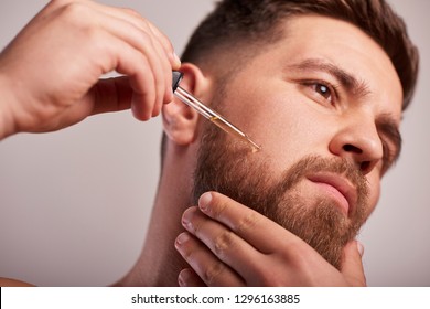 Close-up image of handsome man holding pipette with oil for beard