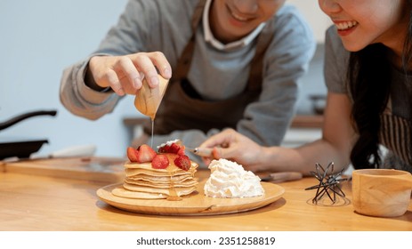 Close-up image of a handsome young Asian man is pouring syrup on pancakes, enjoys cooking pancakes with his girlfriend in the kitchen on the weekend. - Powered by Shutterstock