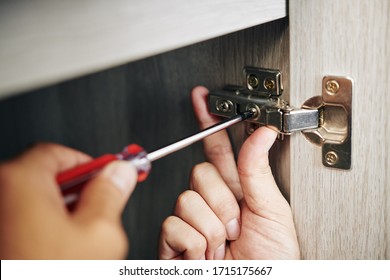 Close-up image of handyman assembling kitchen cabinet and screwing door hinge