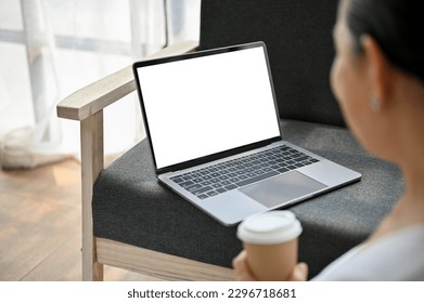 Close-up image of a happy senior woman sipping coffee and using her laptop on sofa in her living room. laptop computer white screen mockup - Powered by Shutterstock