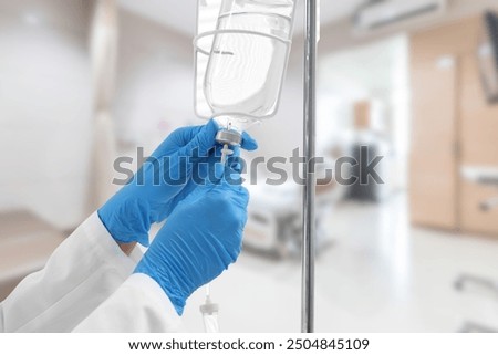 A close-up image of a healthcare professional wearing blue gloves adjusting an IV drip in a hospital setting, with the background showing a blurred patient bed and medical equipment.