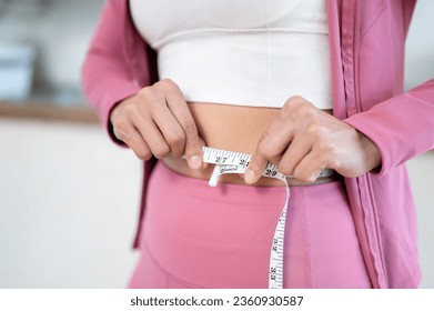 Close-up image of a healthy and slim woman in sportswear measuring her waist with a measuring tape. diet, nutrition, healthy body, workout, body training
