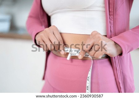 Close-up image of a healthy and slim woman in sportswear measuring her waist with a measuring tape. diet, nutrition, healthy body, workout, body training