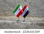 Close-up image of Iran and Iraq flag photographed on cracked concrete floor.
