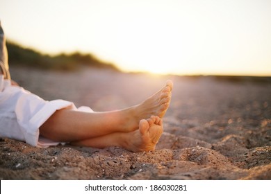 Closeup Image Of Legs Of Senior Woman Sitting Relaxed On Sandy Beach.