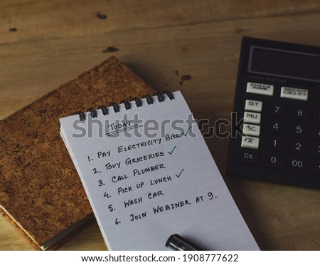 Close-up image of list plan with few jobs done handwritten in small notepad laid on wooden desk. Selective focus, conceptual.