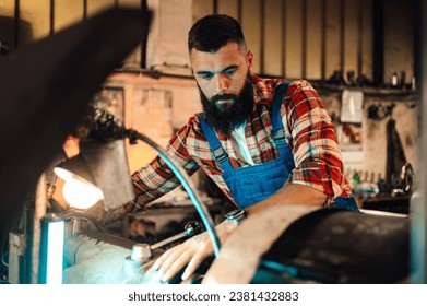 A close-up image of a machinist tinkering on a lather machine, boring a new roll cut metal piece in a factory. Blurred background, foreground. Beard, forearm tattoo, wrist watch - Powered by Shutterstock