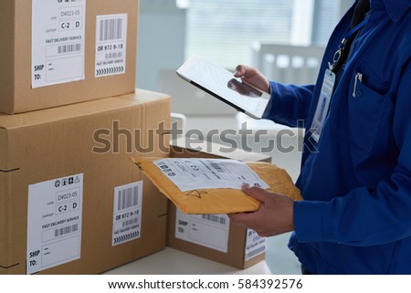 Close-up image of mail worker checking information on parcels