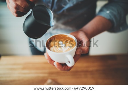 Closeup image of male barista holding and pouring milk for prepare cup of coffee, latte art, vintage color tone, coffee preparation and service concept, lifestyle