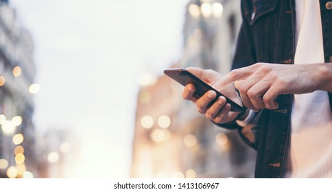 Closeup image of male hands with smartphone at night on city street, searching internet or social networks, hipster man typing an sms message on chat, bokeh lights