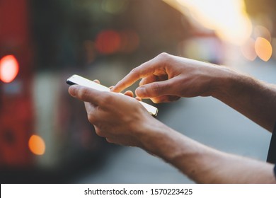 Close-up image of male hands using smartphone at the evening on city at the crossroads, Man typing the messages on social network at the street with sunset on the background - Powered by Shutterstock